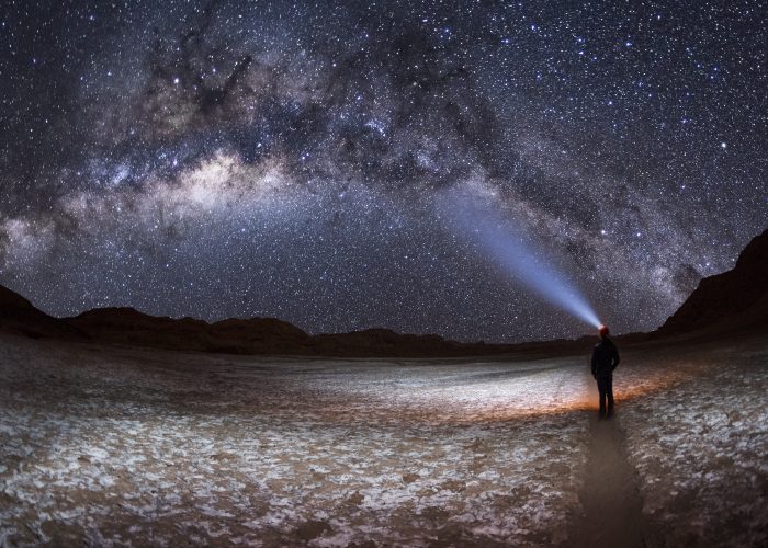 A person at night, shining a light on the Milky Way Galaxy in the Valley of the Moon or Valle de la Luna in San Pedro de Atacama, Chile.